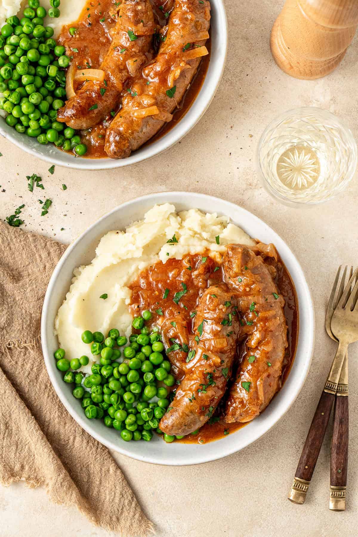 Slow cooker devilled sausages served in bowls on mashed potato with peas.