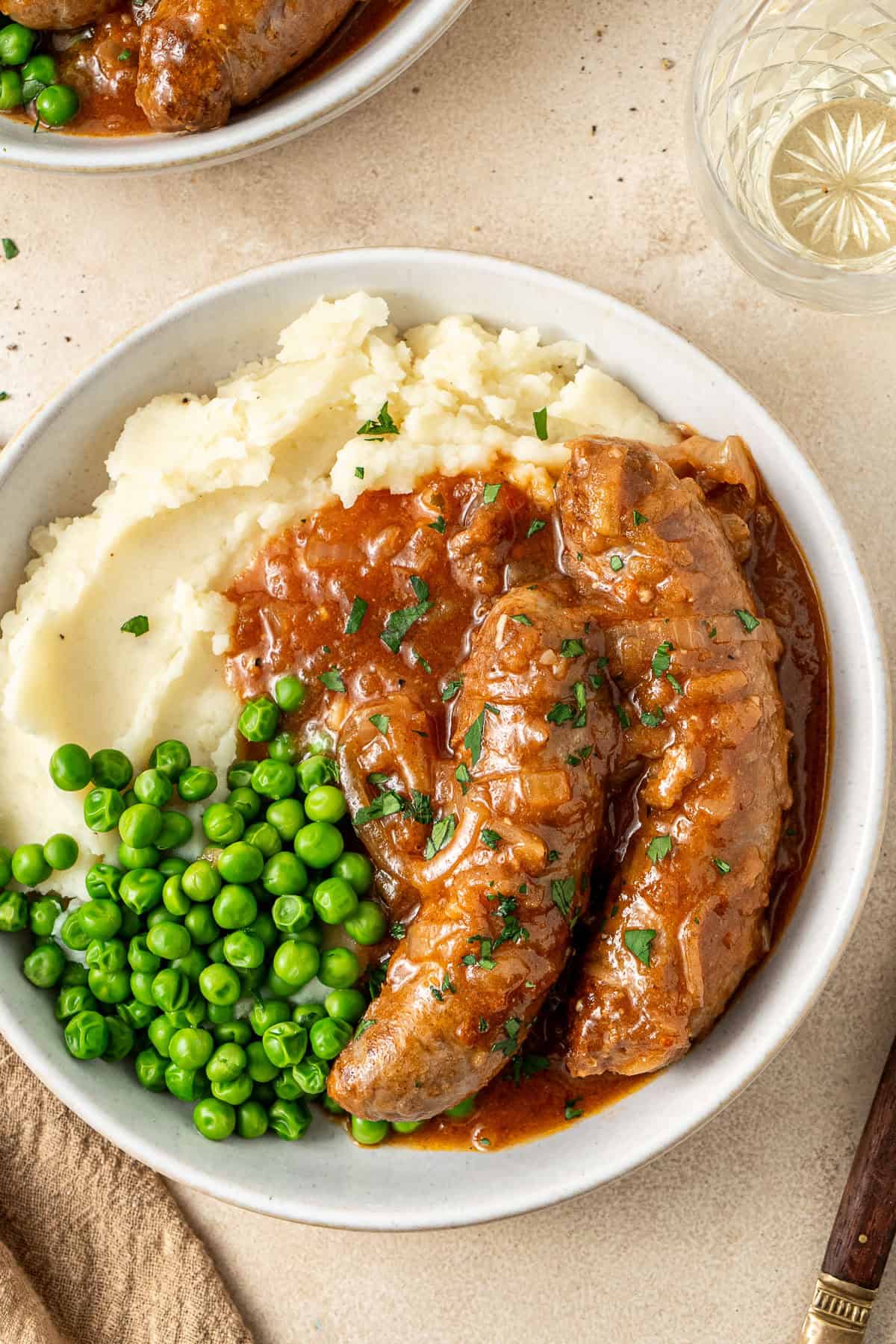 Close up of the sausages served over mash and peas.