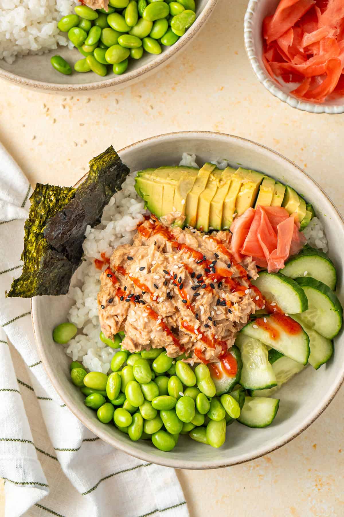 Close up of a spicy tuna sushi bowls with avocado and edamame with seaweed snack sheets.