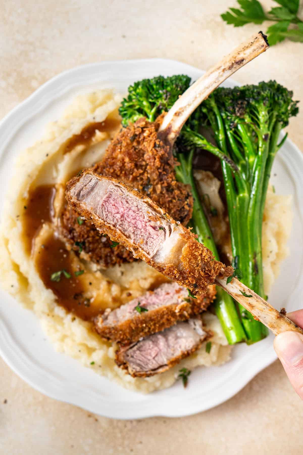 A hand holding up a cutlet cut to show the pink middle of the lamb.