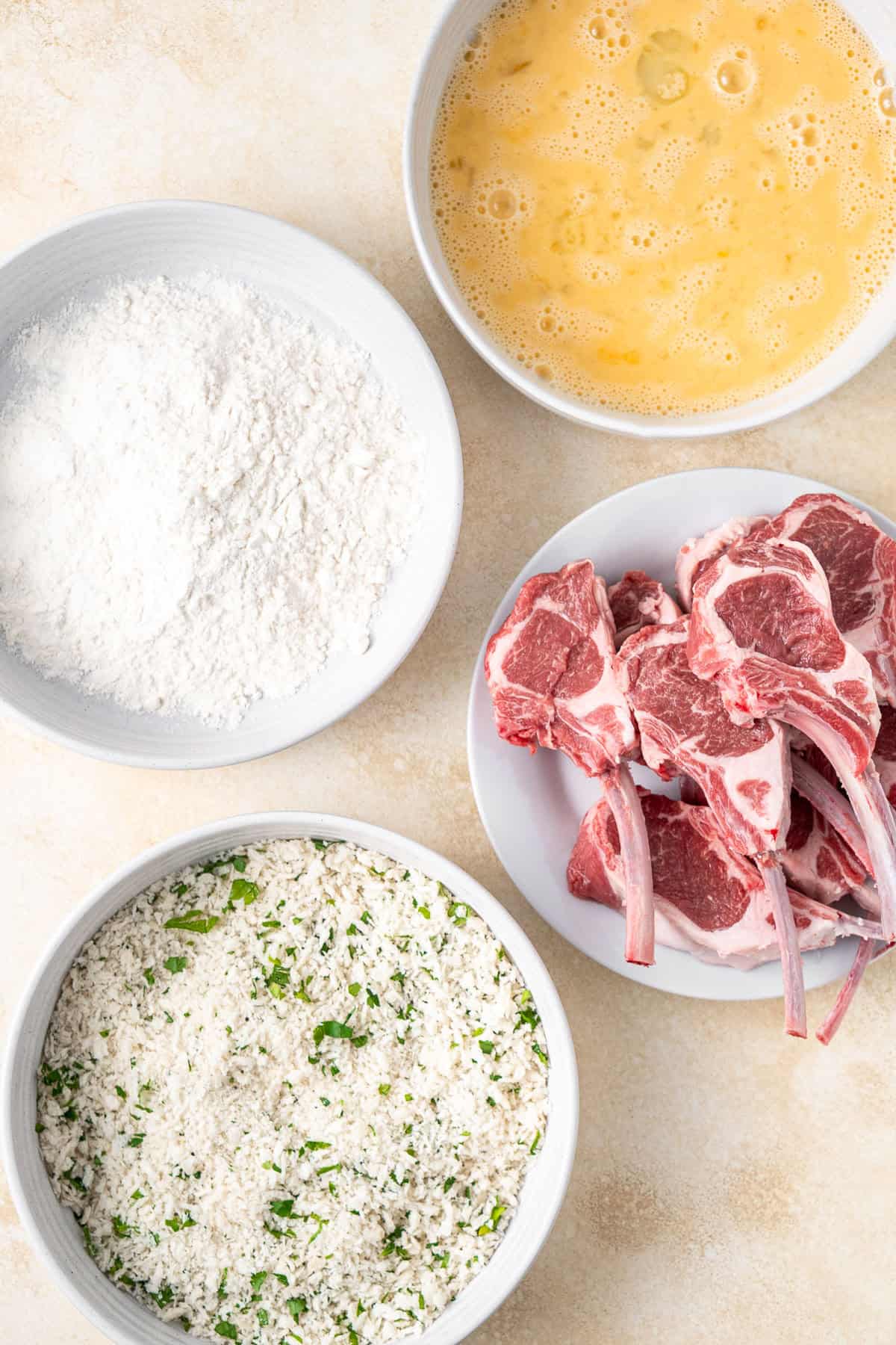 The crumbing station set up with four bowls and the lamb cutlets.