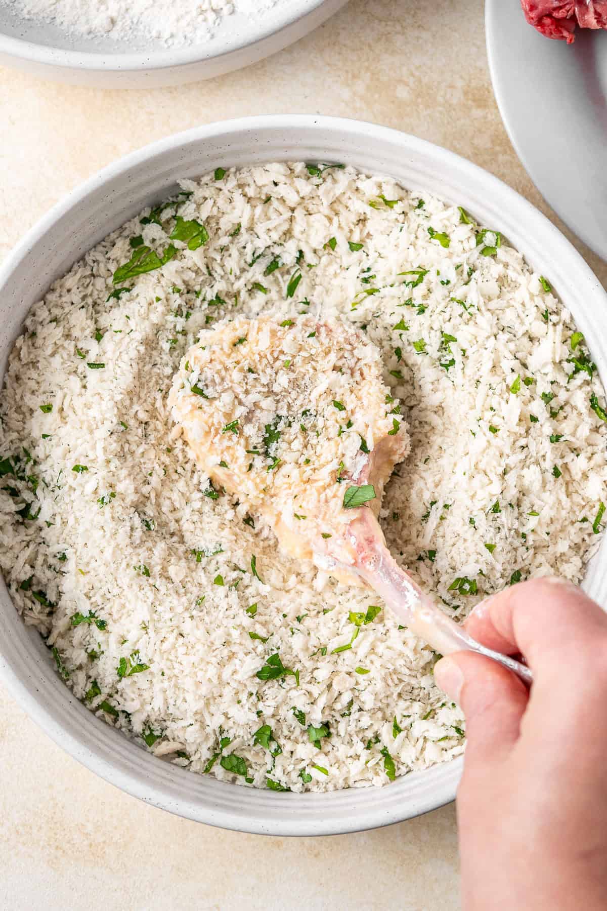 A cutlet being dipped into the crumbs.