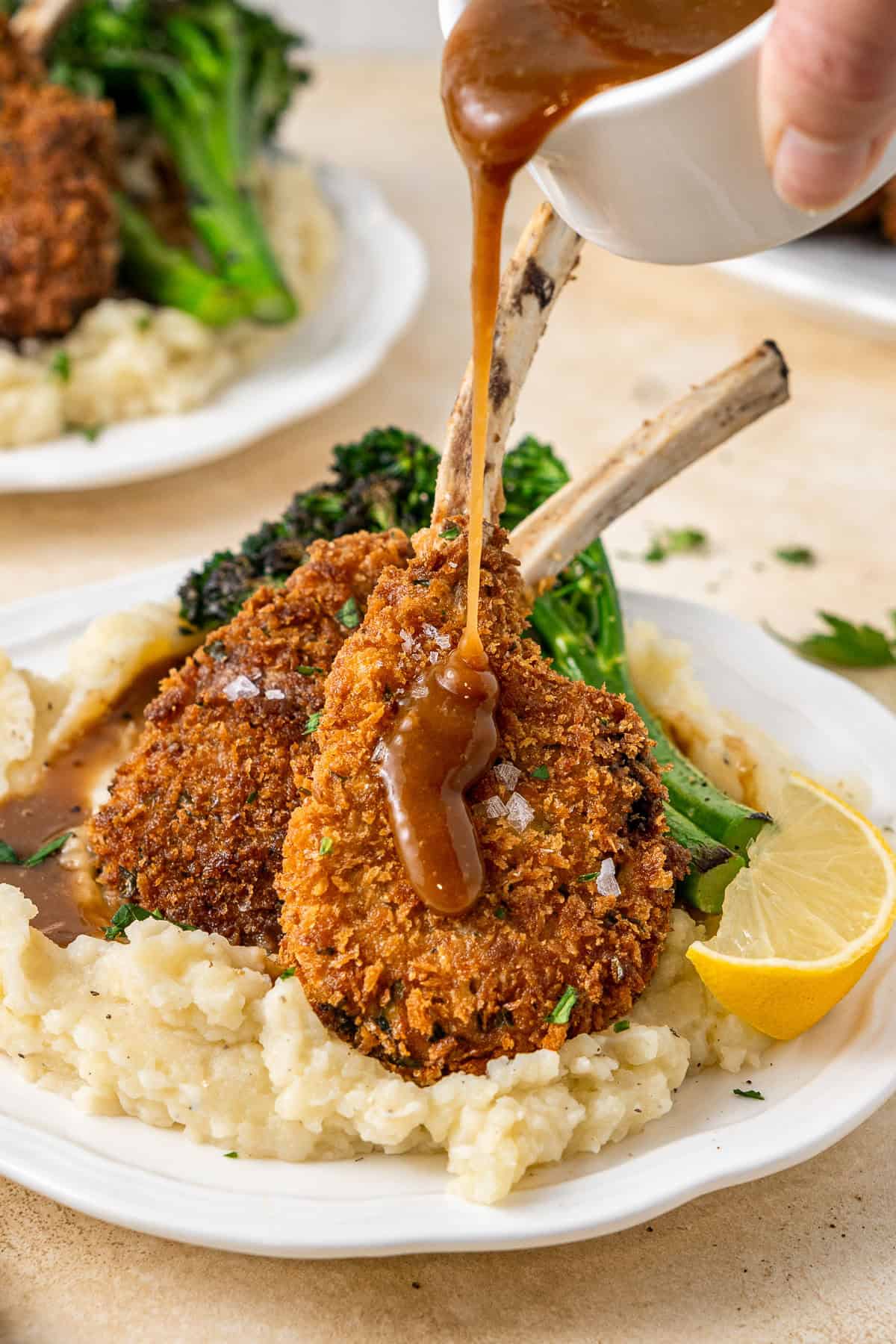 Pouring gravy over the plated cutlets with mash.