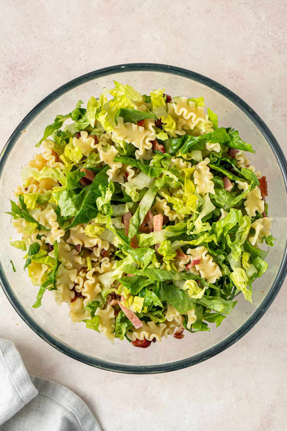 The lettuce, pasta and bacon in a large mixing bowl.