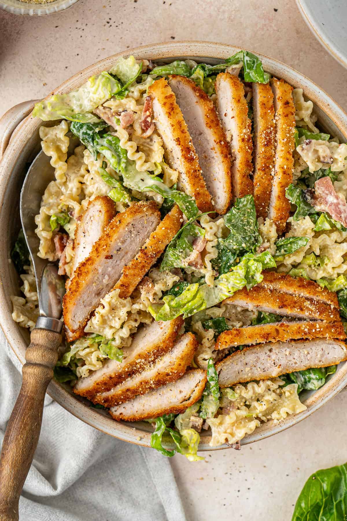 The dairy free chicken caesar pasta salad being served with slices of crispy chicken.