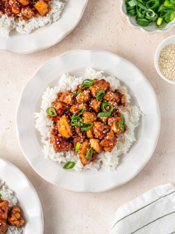 Sweet chilli tofu with rice on white plates with spring onion.