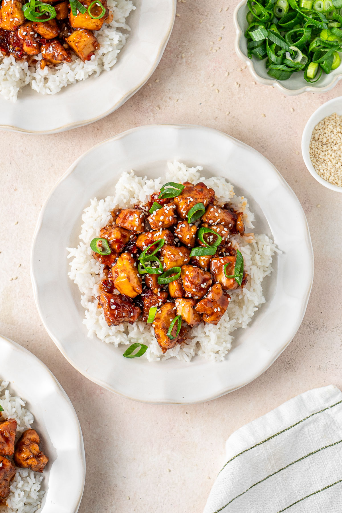 Sweet chilli tofu with rice on white plates with spring onion.