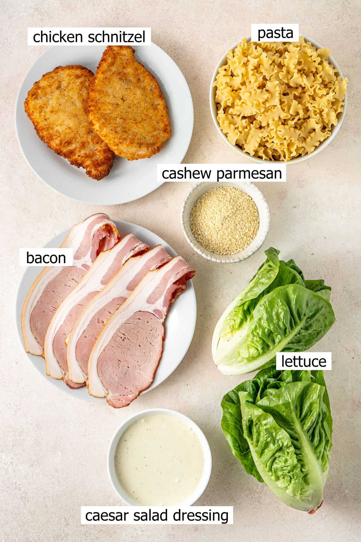 All ingredients needed to make a dairy free caesar pasta salad laid out in bowls.